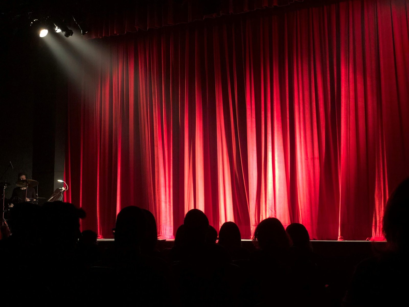 pexels photo 713149 713149 Dimly lit theater stage with red curtains and audience silhouettes under spotlights.